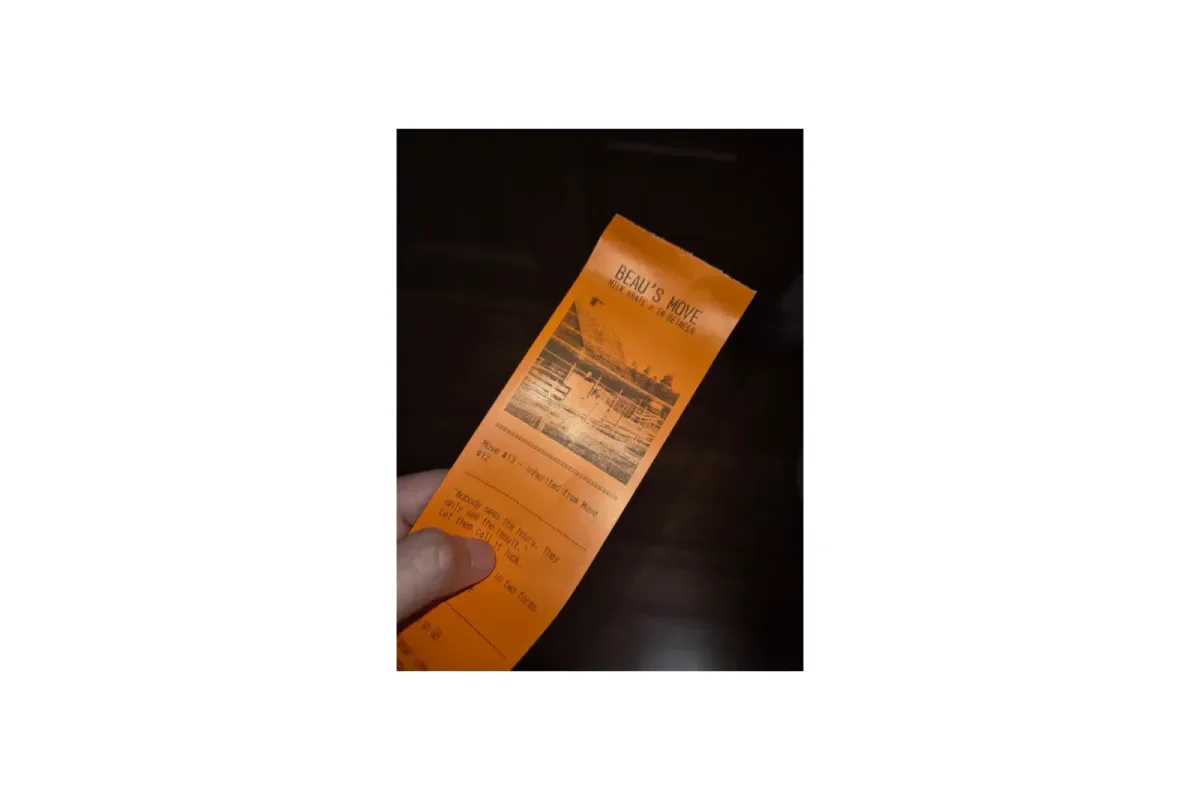A visitor's hand holding an orange Beau's Move receipt, printed with a dithered image and the details of their move.