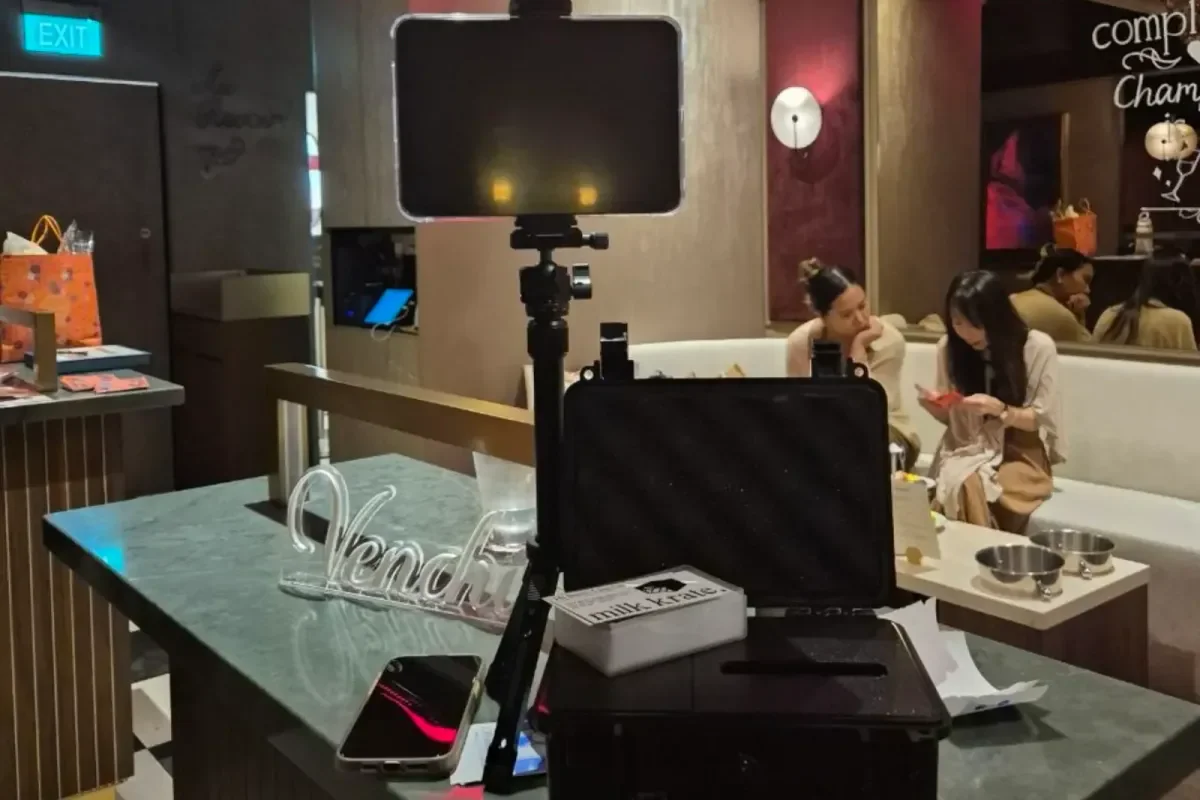 Memory Vault set up on a bar counter at an event: a tablet on a tripod above the black printer case, with guests sitting on a couch behind it.