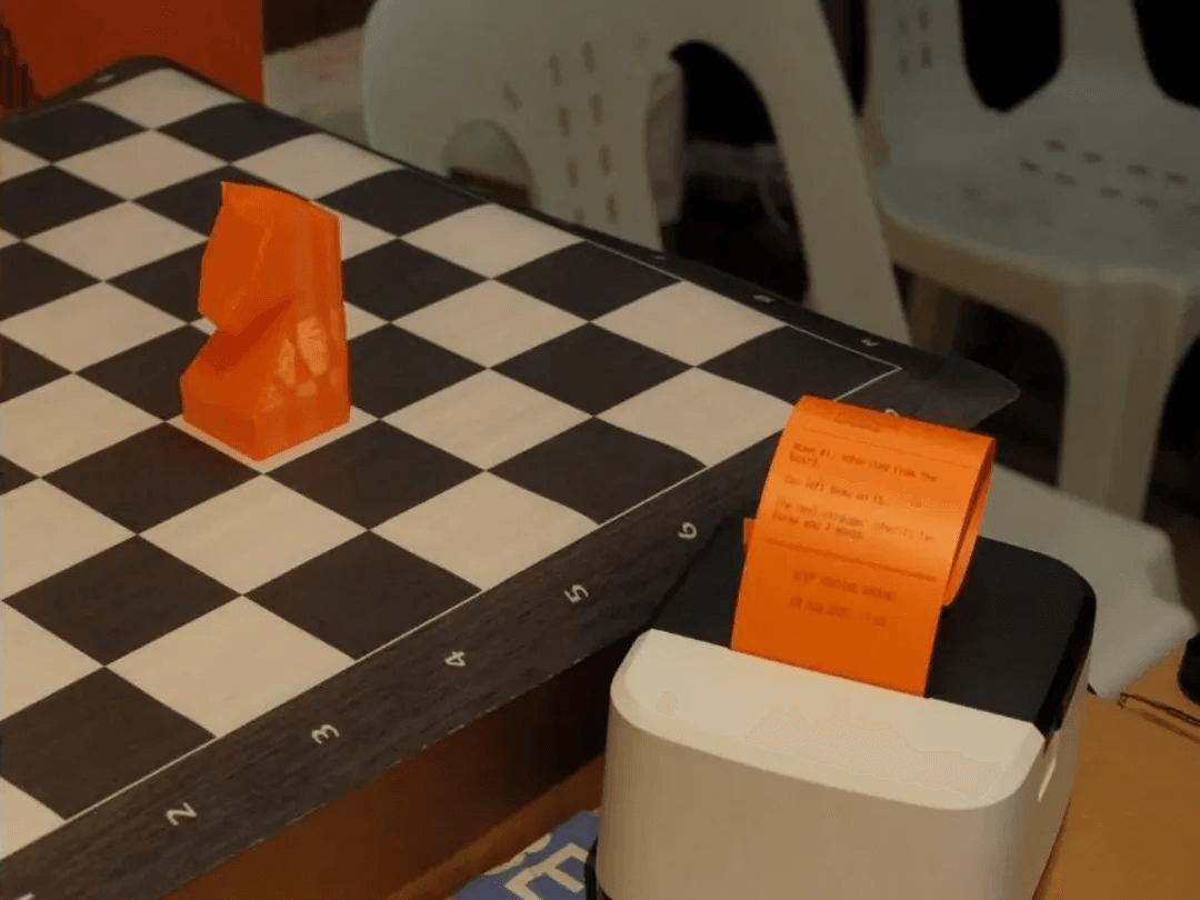 The orange 3D-printed knight on the chessboard, beside a receipt printer feeding out an orange receipt.